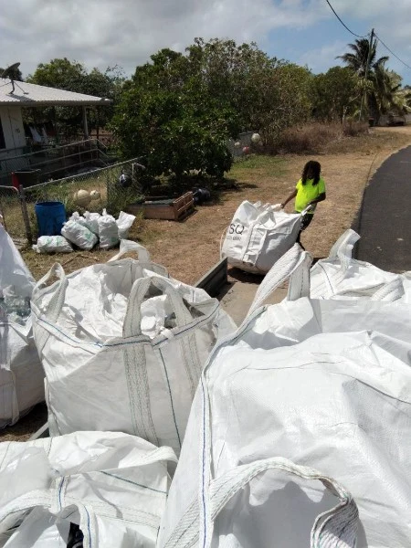 A collection worker moving a large bag towards the trailer.